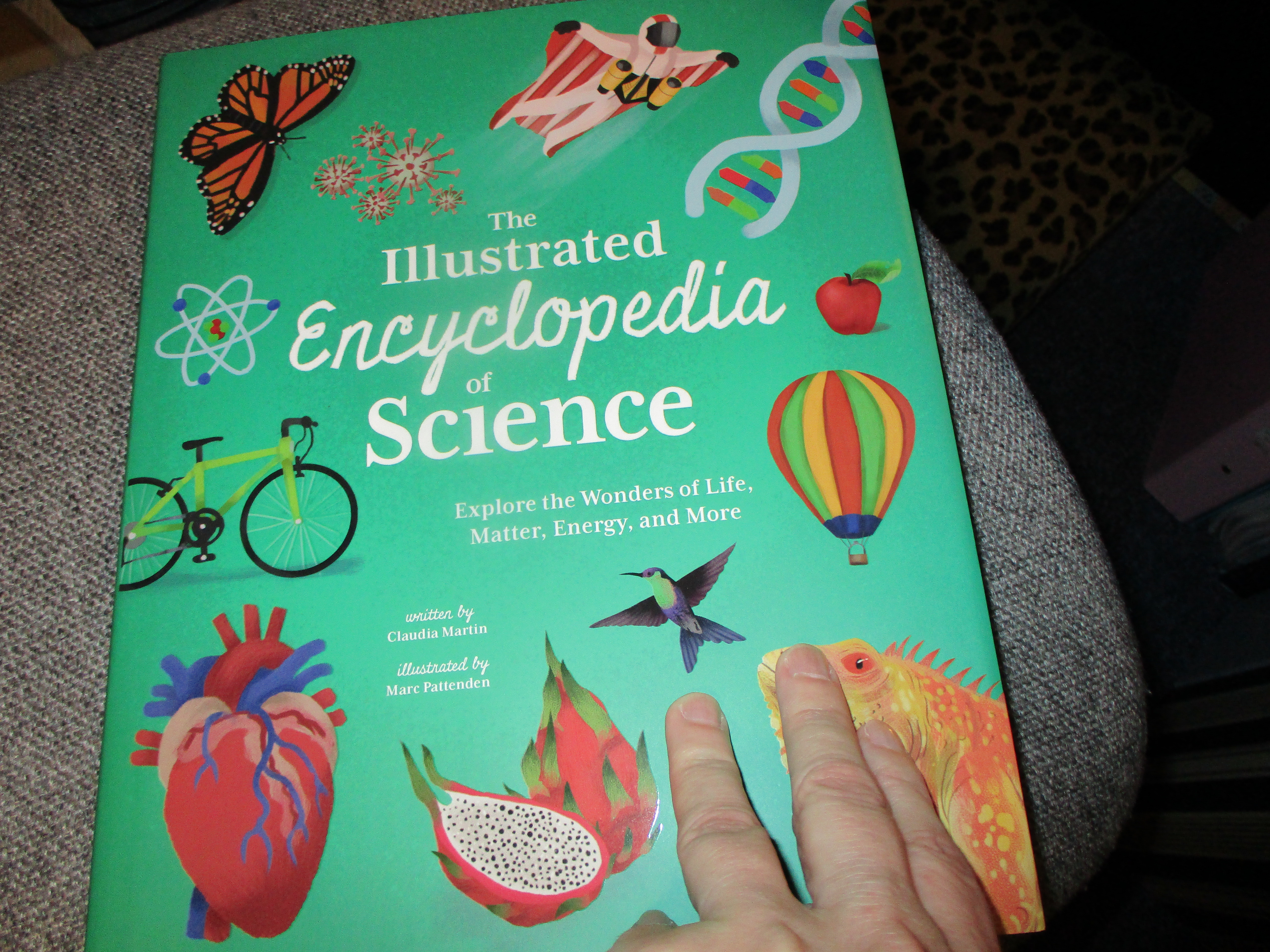 Photo showing Sharon Ann Holgate's hand opening The Illustrated Encyclopedia of Science